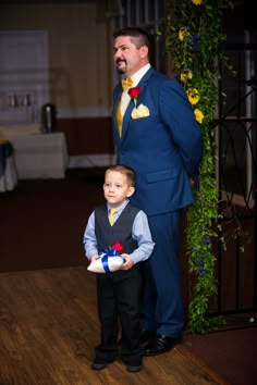 a man in a blue suit and tie standing next to a little boy wearing a red bow tie