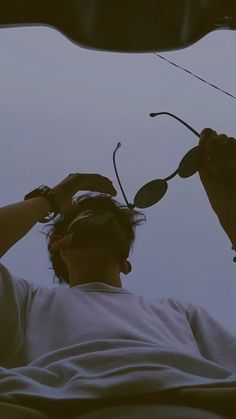 a man is flying a kite in the sky with one hand on his head while another holds it up