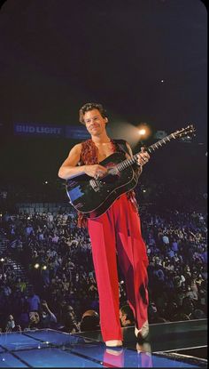 a man standing on top of a stage with a guitar in his hand and an audience behind him