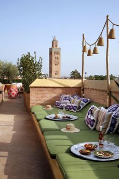 an outdoor seating area with plates and drinks on it, overlooking a clock tower in the distance