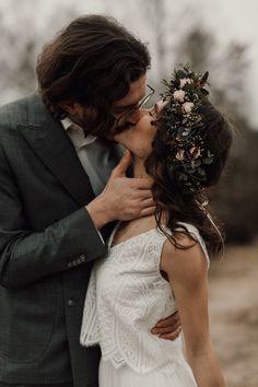 a man and woman kissing each other in front of some trees with flowers on their head