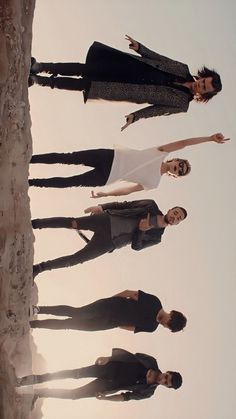 four people standing on the beach with their arms in the air