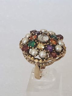 "I'm excited to have come across this beautiful ring because it is in a bigger size and has lots of jewels. The metal is gold plated with a large undercarriage with holes. Each stone is prong set and are in different colored gemstones. The ring has a hallmark \"NB NICKY BUTLER\" and has its original ring box. All stones are intact with non-missing. The ring was used a couple of times and then put away. The finish is shiny with no scratches or other oddities. Makes a great cocktail ring for the H Heirloom Multicolor Ring Jewelry, Vintage Multicolor Jewelry With Stone Setting, Heirloom Multi-stone Pearl Ring Gift, Heirloom Multi-stone Pearl Ring As Gift, Antique Multi-stone Cluster Jewelry, Antique Gold Cluster Ring With Multi-stone, Antique Multicolor Multi-stone Jewelry, Antique Multi-stone Cluster Ring As Gift, Vintage Multi-stone Cluster Ring