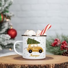 a mug with candy canes in it sitting on top of a tree stump next to a christmas tree