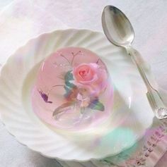 a white plate with a pink rose on it next to a silver spoon and fork