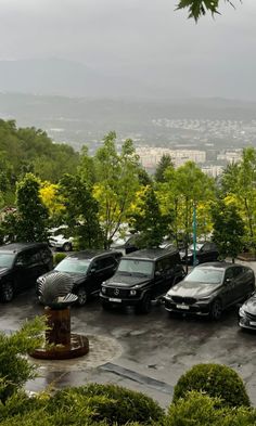 a parking lot filled with lots of parked cars next to lush green trees and bushes