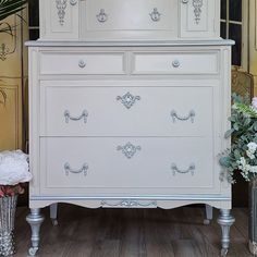 a white dresser sitting on top of a wooden floor next to a vase with flowers