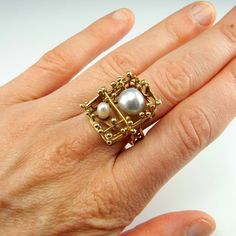 A custom made artisan ring in solid 14K yellow gold and set with two baroque salt water pearls. This ring dates to the 1970s and is in lovely condition ready to gift or to wear. The design is one of a kind and it is completely handmade with no cast or machined components. It is a big ring with the top of the ring measuring 13/16" long by 11/16" wide by 9/16" tall (21mm x 18mm x 15mm). In total it weighs 9 grams. On the inside of the shank is clearly marked 585 for 14K gold and also signed by the Unique Gold Pearl Ring For Formal Occasions, Heirloom Style Gold Pearl Open Ring, Heirloom Gold Pearl Open Ring, Unique 14k Yellow Gold Pearl Ring, Unique Yellow Gold Pearl Ring For Anniversary, Pearl Gold Ring, Brutalist Jewelry, Pearl Cocktail Ring, Pearl Anniversary