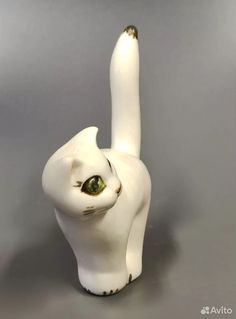 a white ceramic cat with green eyes on a gray background, looking up at the viewer