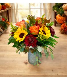 a vase filled with sunflowers and other flowers on a wooden table next to pumpkins