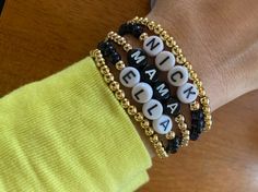 the bracelets are decorated with letters and beads on each one hand, while the other is wearing a yellow shirt