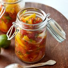 two jars filled with different types of food on top of a wooden table next to spoons