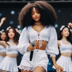 a group of women in white outfits on stage with one woman singing into a microphone