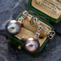 two pairs of pearl earrings in a green box on top of some rocks and gravel