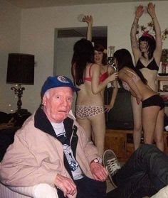 an old man sitting on a couch in front of some women with their arms up