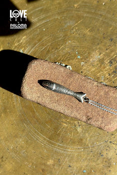 Silver fish pendant hanging from a silver chain head down laying on a brick-like stone on a brass surface. Antique Silver Hand Cast Sterling Silver Necklace, Hand Cast Antique Silver Sterling Silver Necklace, Hand Cast Sterling Silver Necklace In Antique Silver, Sterling Silver Fish-shaped Jewelry Gift, Sterling Silver Fish-shaped Jewelry As Gift, Handmade Silver Fish-shaped Necklace, Handmade Sterling Silver Fish-shaped Jewelry, Handmade Sterling Silver Fish Jewelry, Sterling Silver Fish-shaped Necklace With Lobster Clasp