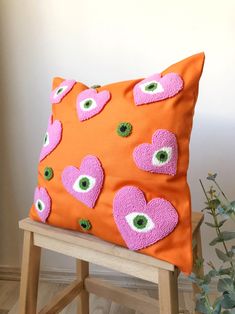 an orange pillow with pink and green eyeballs on it sitting on a wooden chair