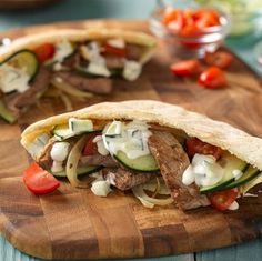 two pita sandwiches on a cutting board with tomatoes and cucumbers