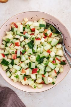 a bowl filled with cucumbers and red peppers next to a pair of spoons