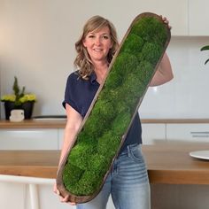 a woman holding a large green pillow in the shape of a rectangle with moss growing on it