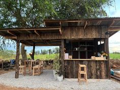 an outdoor bar made out of wood with chairs around it and a tree in the background