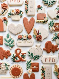 many different decorated cookies are arranged on a white table top with flowers and leaves around them