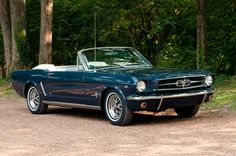 an old blue mustang convertible parked in the woods