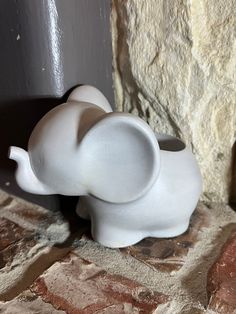 a small white elephant figurine sitting next to a stone wall