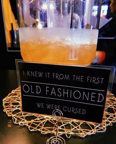 an old fashioned drink is sitting on a table with a sign that says, i knew it from the first old fashioned we were curious