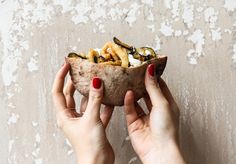 two hands holding a bowl filled with food on top of a white wall covered in peeling paint