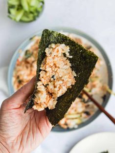 someone holding up a piece of sushi with rice and broccoli in the background