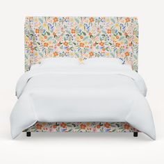 an upholstered bed with white linens and flowers on the headboard is shown