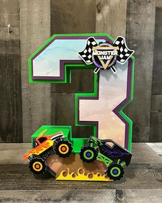 the number three is made out of cardboard and has two monster trucks on it,