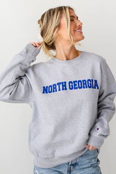 Calling all North Georgia residents, the Heather Grey North Georgia Sweatshirt was made just for you! This comfy sweatshirt is designed with a soft and stretchy knit with a fleece interior. It features a crew neckline, long sleeves, a relaxed fit, and the words "North Georgia" on the front. Style the Heather Grey North Georgia Sweatshirt with your favorite denim and sneakers for a casual look! Soft + Stretchy Knit Fabrication Fleece Interior "North Georgia" Graphic Crew Neckline Long Sleeves Rel Georgia Sweatshirt, Woodstock Georgia, Baseball Sweatshirts, Letter Sweatshirt, Champion Brand, University Sweatshirts, Exclusive Dress, North Georgia, Champion Sweatshirt