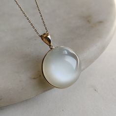 ITEM DESCRIPTION: >>The pendant is made from Solid 14K Yellow Gold. Gemstone used is absolutely natural and ethically sourced.  >>Natural White Moonstones cabochon cut and round shape with bezel setting are studded on it with utmost precision.  >>This is a minimalist design and is absolutely hassle-free and everyday jewelry.  ✓ Gem: White Moonstone ✓ Gem size: 23x23 mm round  ✓ Gem weight: 34.30 carats ✓ Gold purity: 14K (58.33% approx.) ✓ Gold weight: 0.76 grams  ✓ Gross weight: 7.62 grams The Gold purity is guaranteed and it comes with authentic 14K gold hallmark. Since these Pendants are handmade, they are Nickel/Lead FREE.  CUSTOMIZATION: --> You can choose your own gemstone as well. --> The same pendant can be made in thicker bezel as well. --> Kindly drop a message for the same. CUST 14k Gold White Jewelry With Si Clarity, White Moonstone Ring With Si Clarity, White 14k Gold Jewelry With Round Stone, Formal Moonstone Round Necklace, Formal Round Moonstone Necklace, White Moonstone Necklace For Formal Occasions, Formal White Moonstone Necklace, White Gold Moonstone Round Pendant Jewelry, White Gold Polished Moonstone Jewelry