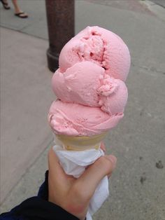 a hand holding an ice cream cone with pink icing