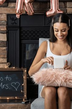 a woman sitting in a chair holding a cup and looking at her phone while smiling