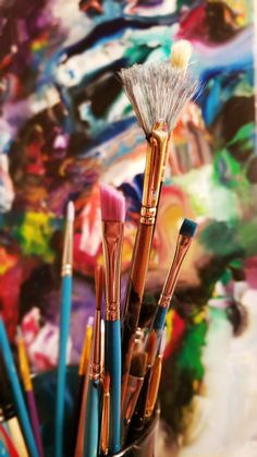 brushes are in a cup with paintbrushes on the table next to an abstract painting