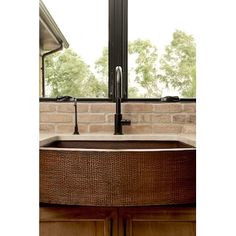 a brown sink sitting under a window next to a wooden cabinet and counter top in front of a brick wall