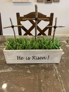 a wooden planter with grass in it that says he is risen