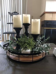 three candles sitting on top of a table with greenery in front of the fire place