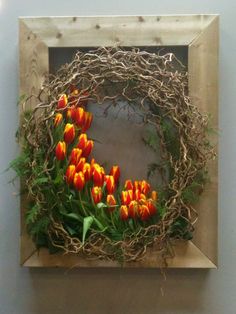 an arrangement of orange and yellow tulips in a wooden frame on the wall