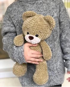 a person holding a brown teddy bear in their hands and wearing a gray sweater with white trim