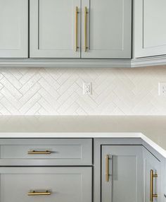 a kitchen with gray cabinets and gold pulls on the handles, white marble countertops and herringbone backsplash