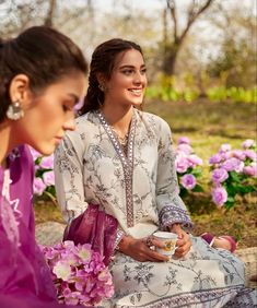 two women are sitting on the ground and one is holding a cup in her hand