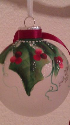 a glass ornament with holly leaves and red berries on it hanging from a ceiling