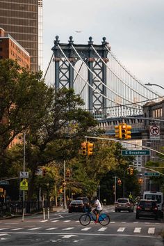 a man riding a bike across a street in front of a bridge and traffic lights