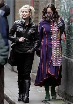 two women are walking down the street in leather jackets and boots, one is wearing a purple coat