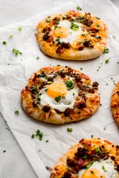 four small pizzas with eggs on them sitting on wax paper