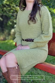 a woman sitting on top of a wooden bench in a green sweater and brown boots